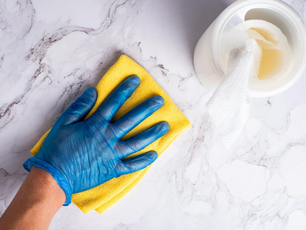Hand in blue glove wiping a white marble surface with a yellow cloth.